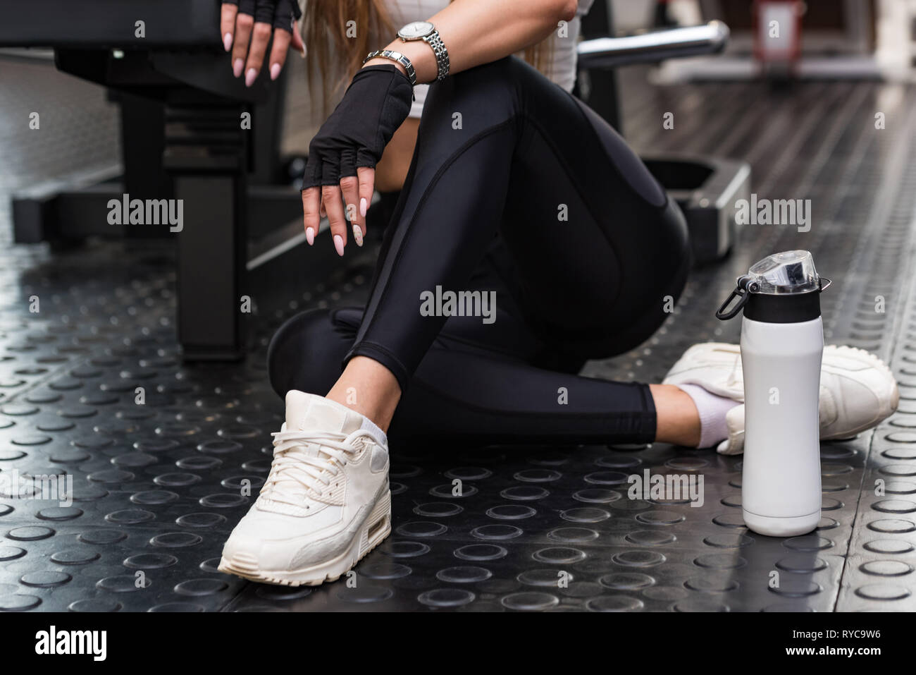 Attraktive fitness Modell sitzt mit Fitness Drink in einem modernen Fitnessraum. Unteren Teil anzeigen Stockfoto