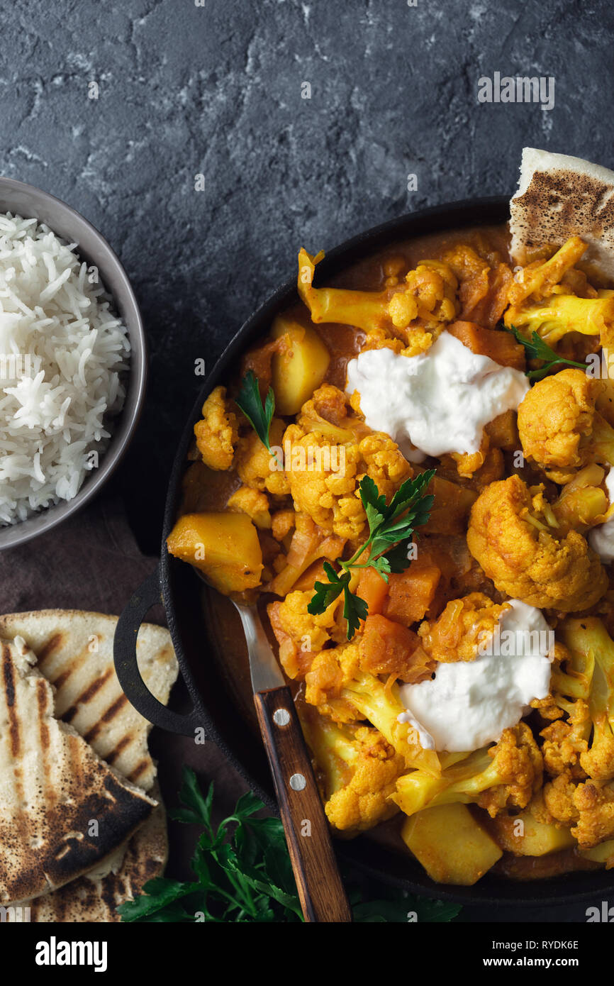 Vegetarisches indisches Essen. Blumenkohl curry mit Basmatireis und Naan Brot auf dunklem Stein Hintergrund der Ansicht von oben. Gesundes und schmackhaftes Essen Konzept Stockfoto