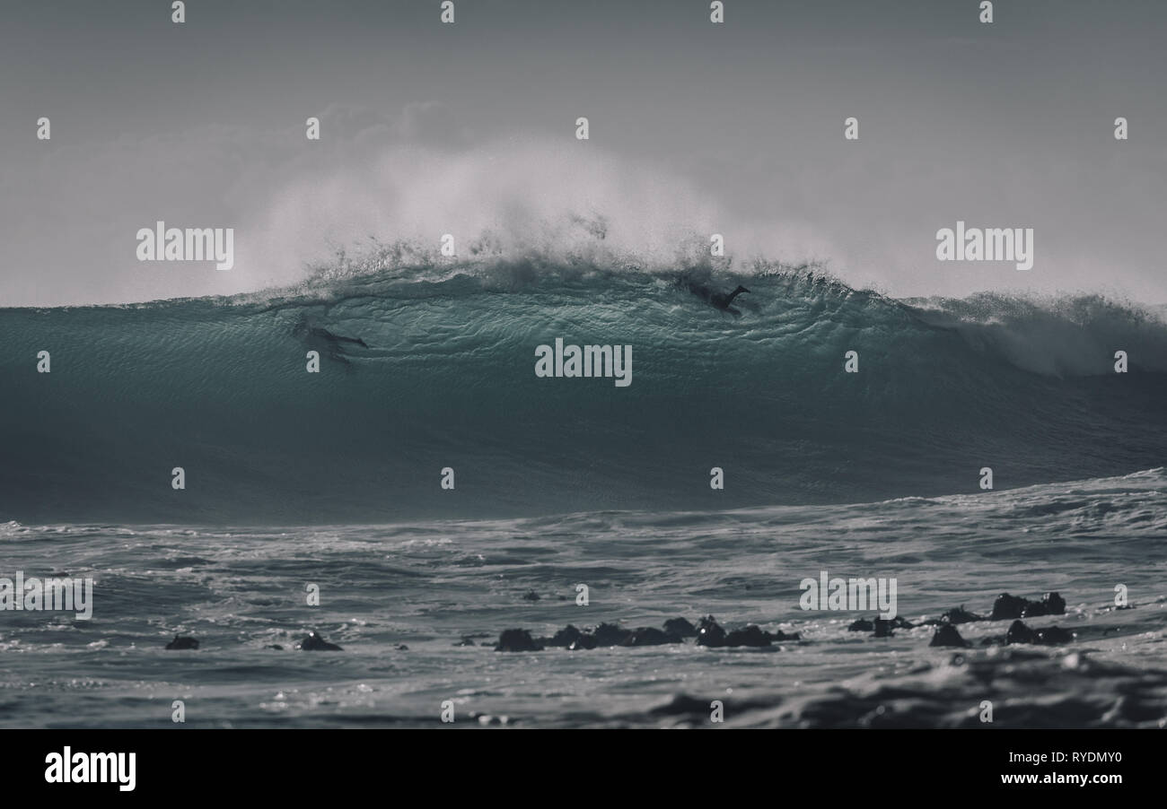 Zwei Surfer schwimmen durch ein großes, hintergrundbeleuchtetes Wave in Kapstadt Stockfoto