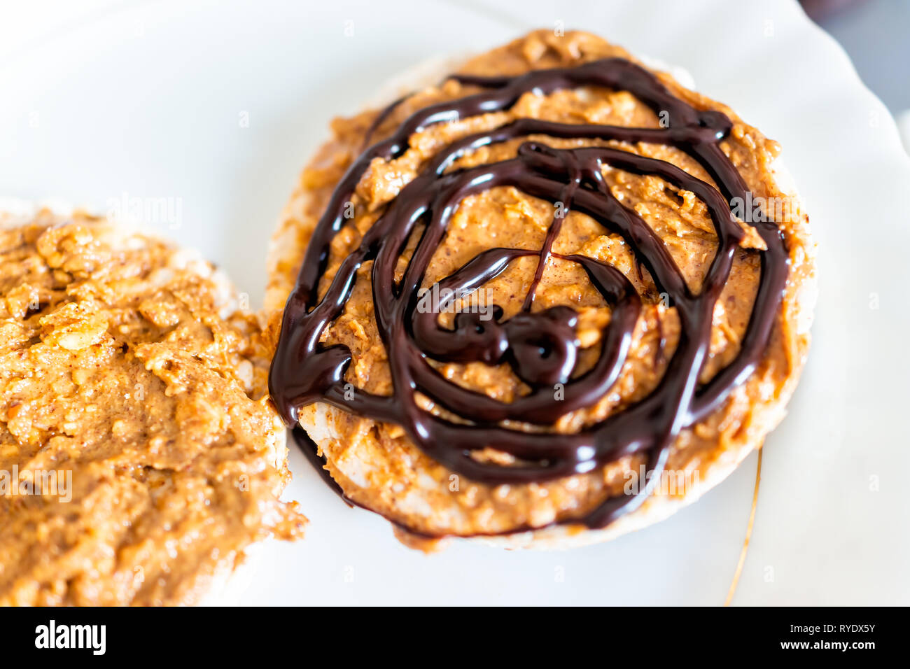 Flache Oberseite closeup von Reis Kuchen mit Schokolade Soße beträufeln oder Sirup vegan Vegetarische snack Dessert ein einziges Stück auf weiße Platte und Erdnussbutter Stockfoto