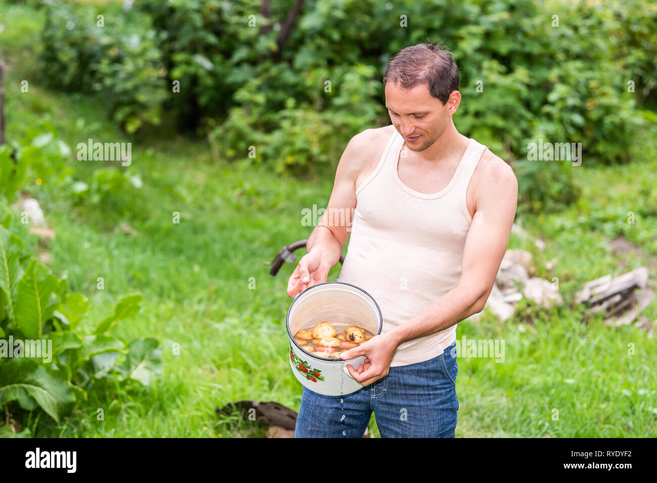 Junger Mann Landwirt in Garten spülen Schmutz von homegrown waschen Kartoffeln im Topf grün Sommer in Bauernhof außerhalb Stockfoto