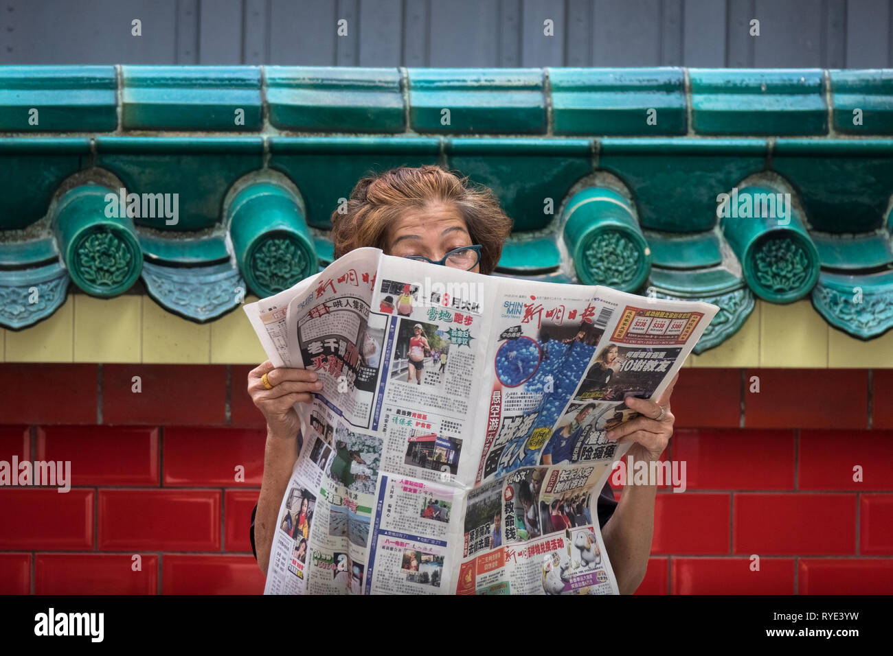 Alte Singapur Frau liest Zeitung auf Straße an chinesischen Tempel - Singapur Stockfoto