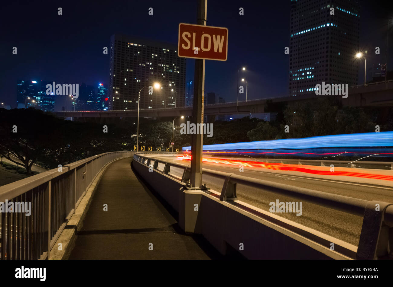 'Langsam' Schild mit langen Belichtung Auto Rückleuchten und Singapur Gebäude Stockfoto