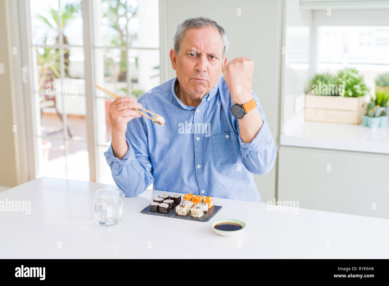 Gut aussehender älterer Mann mit Stäbchen zu Essen zum Mitnehmen zu Hause genervt und frustriert schrie mit Zorn, verrückt und schreien mit erhobener Hand Sushi, eine Stockfoto