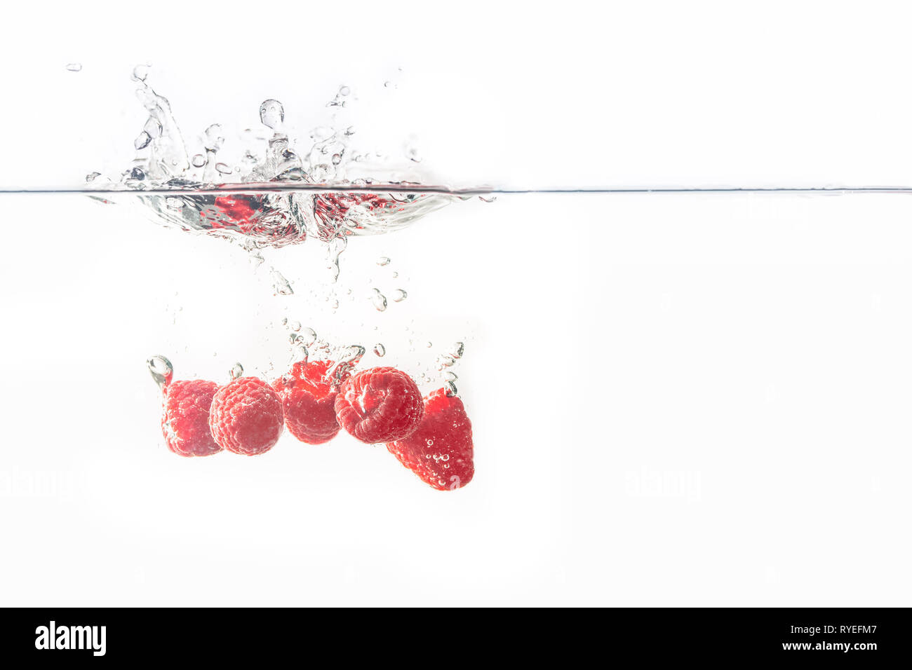 Bündel von saftig lecker aussehenden Himbeeren Spritzer in die Wasseroberfläche und Untergang. Auf weißem Hintergrund, Splash essen Fotografie. Stockfoto