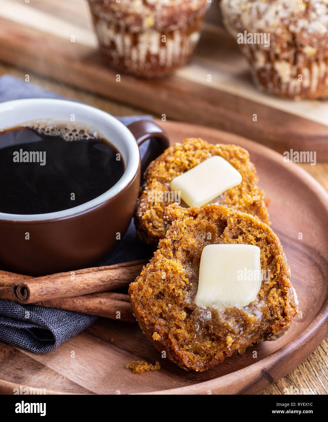 Pumpkin Muffin in der Hälfte mit schmelzender Butter und eine dampfende Tasse Kaffee auf einer Holzplatte Stockfoto
