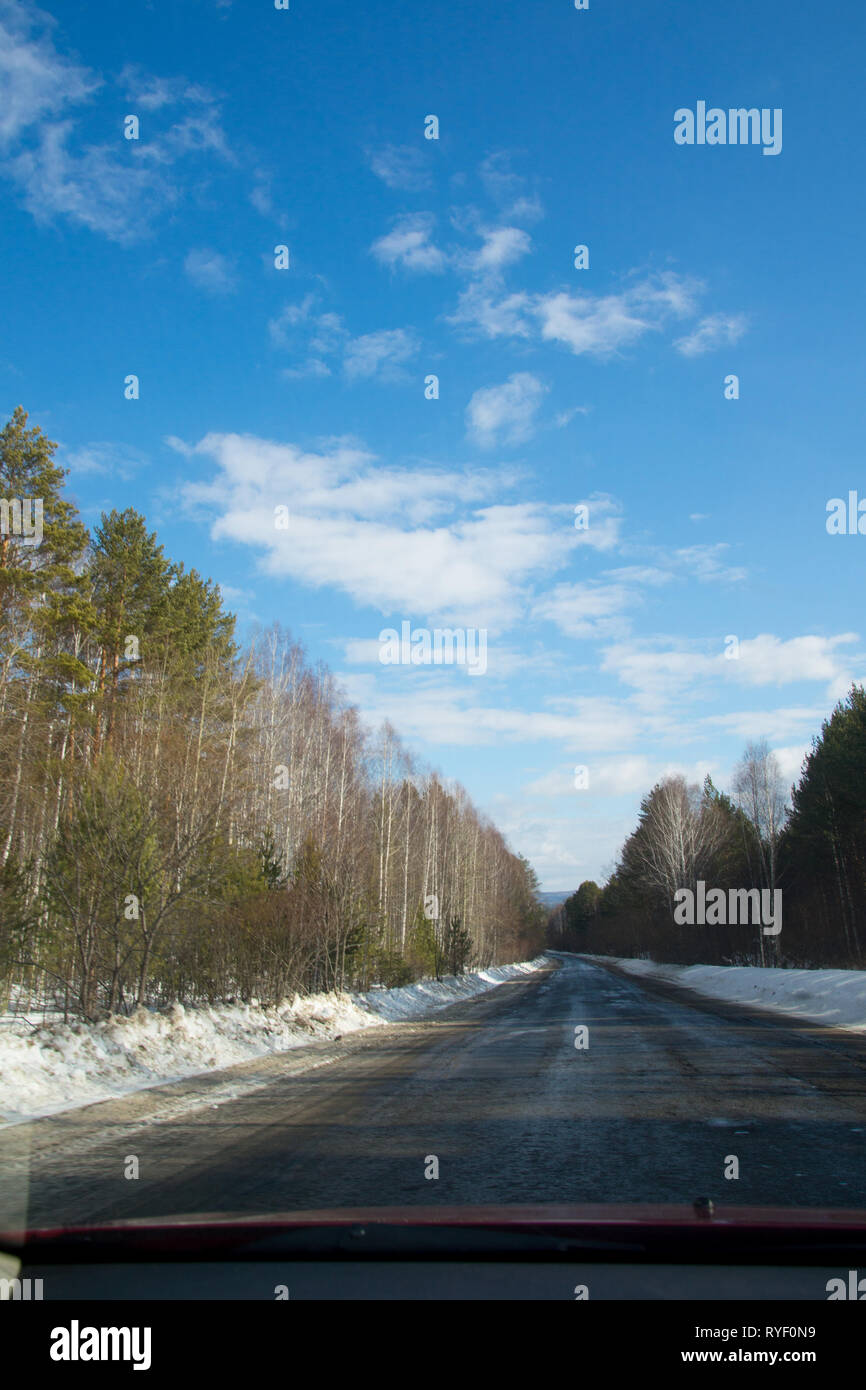 Blick auf die Straße durch die Windschutzscheibe. Frühjahr Wald. Nasse Straße. Blauer Himmel mit Wolken. Fahrerseite Sicht Sicht durch Auto windshiel Stockfoto