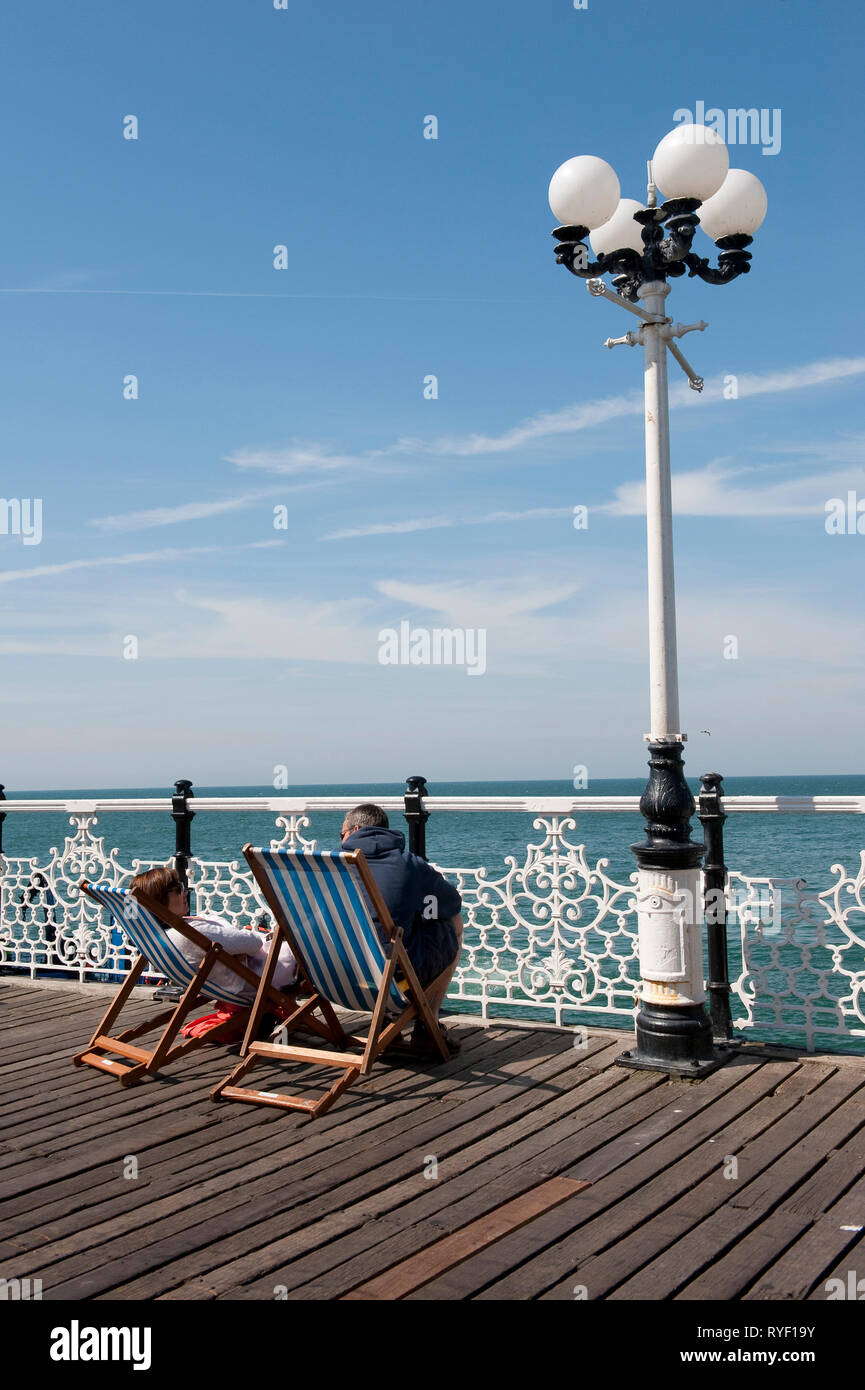 Paar in Liegestühlen Palace Pier von Brighton, Brighton, Sussex, England sitzen. Stockfoto