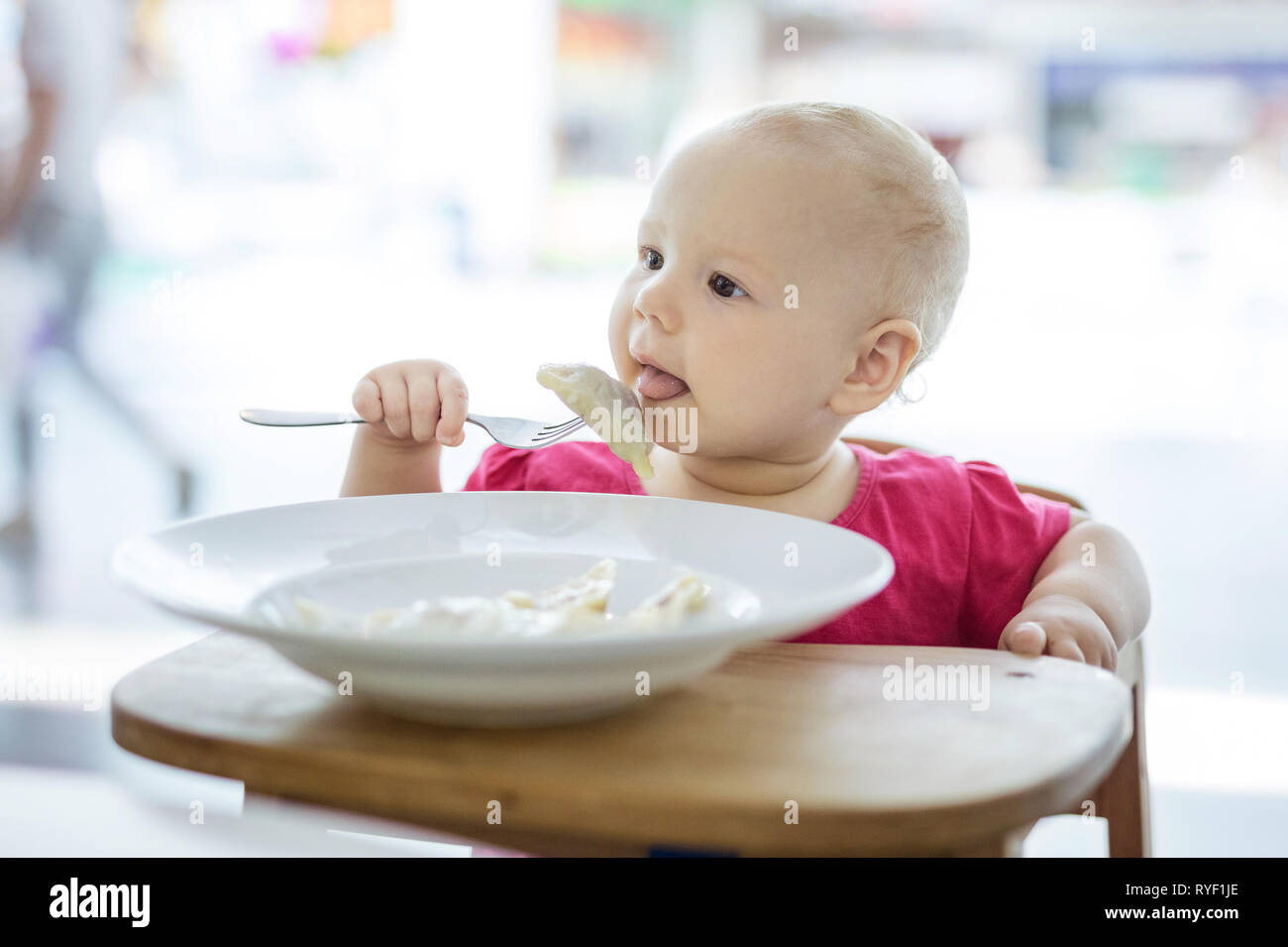 Süße kleine Mädchen im Hochstuhl sitzen und Knödel Essen Stockfoto