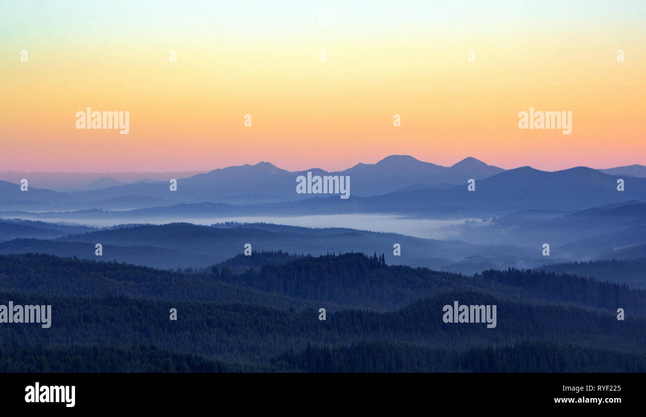 Nebeliger morgen in den Bergen mit Silhouetten der Berge. Serenity sunrise mit weichen Sonnenlicht und Schichten von Haze. Berglandschaft mit Nebel im Wald Stockfoto