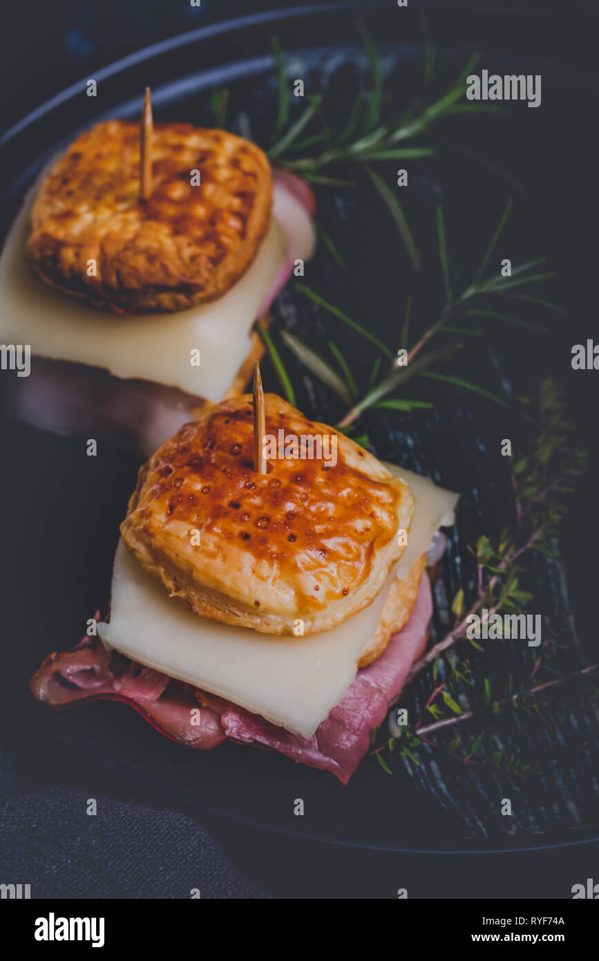 Vertikale Foto mit zwei Sandwiches. Sandwiches sind aus Blätterteig Teig Quadrate mit Käse gefüllt und getrocknetem Schinken. Essen ist auf schwarze Platte mit platziert Stockfoto