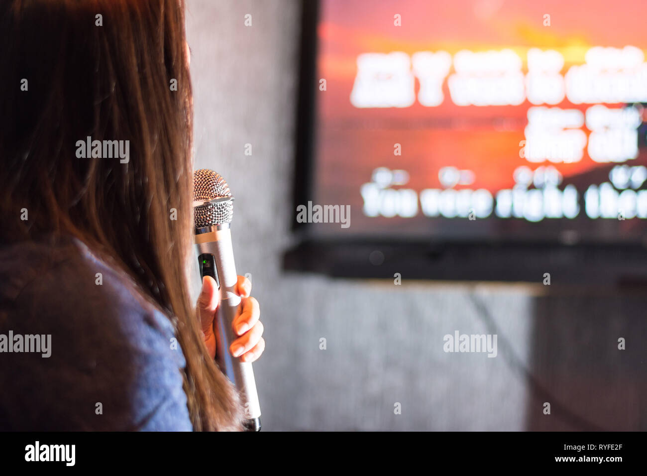 Eine Frau in der Karaoke Bar hält ein Mikrofon vor TV-Bildschirm mit Lyrics. Stockfoto
