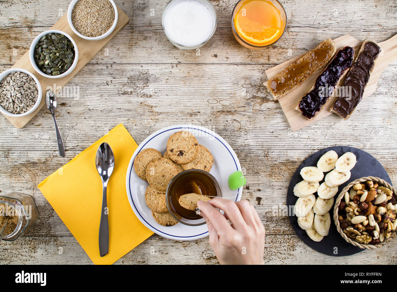 Eine Frau hand Einweichen der Keks in Kaffee an einem Holztisch zum Süßen Veganes Frühstück Schuß von oben mit Bananenscheiben, gemischte getrocknete Früchte, Gemüse Stockfoto