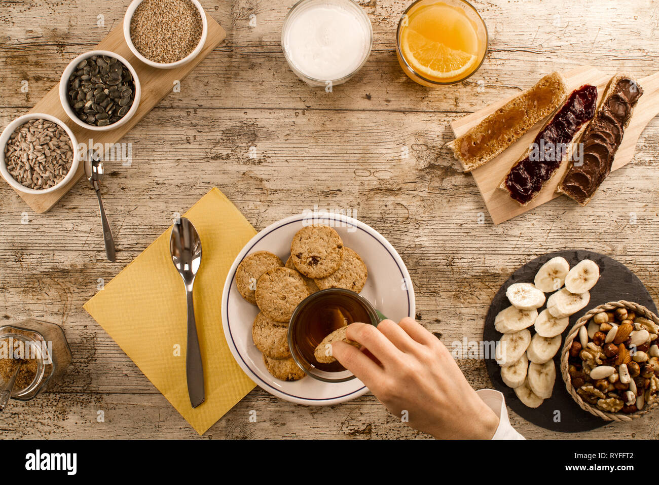Eine Frau hand Einweichen der Keks in Kaffee an einem Holztisch zum Süßen Veganes Frühstück Schuß von oben mit Bananenscheiben, gemischte getrocknete Früchte, Gemüse Stockfoto
