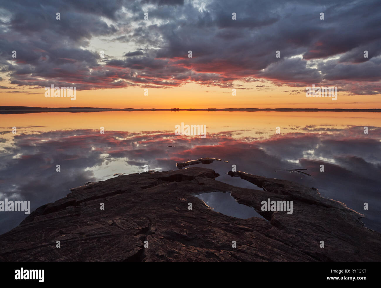 Sonnenuntergang mit Crimson Red Farbe in die Wolken und die Felsen am Ufer. Dramatische Reflexion der Sonne im Wasser eines Sees in Finnland. Stockfoto