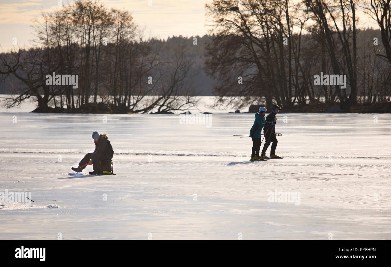 Fernverkehr ice Skaters skating Vergangenheit Frau angeln durch das Loch im Eis auf dem See Malaren, Schweden, Skandinavien Stockfoto