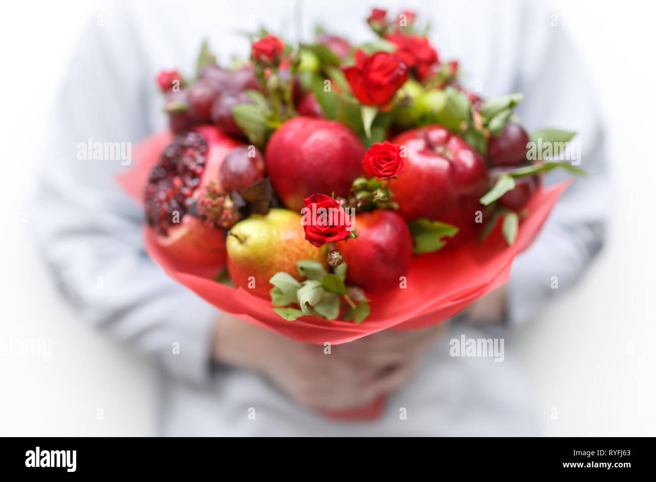 Genießbare Blumenstrauß aus Granatapfel, Äpfel, Pflaumen und roten Rosen in die Hände der Frau auf weißem Hintergrund Stockfoto