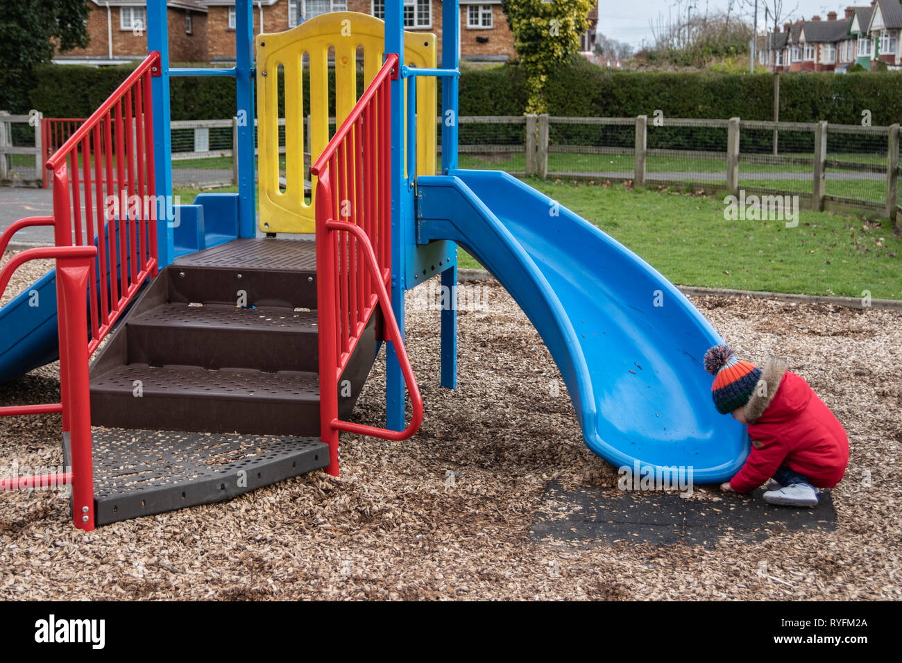 Zwei Jahre alten Jungen spielen auf dem Kunststoff Folie im Park trägt einen roten Mantel und Bobble hat Stockfoto