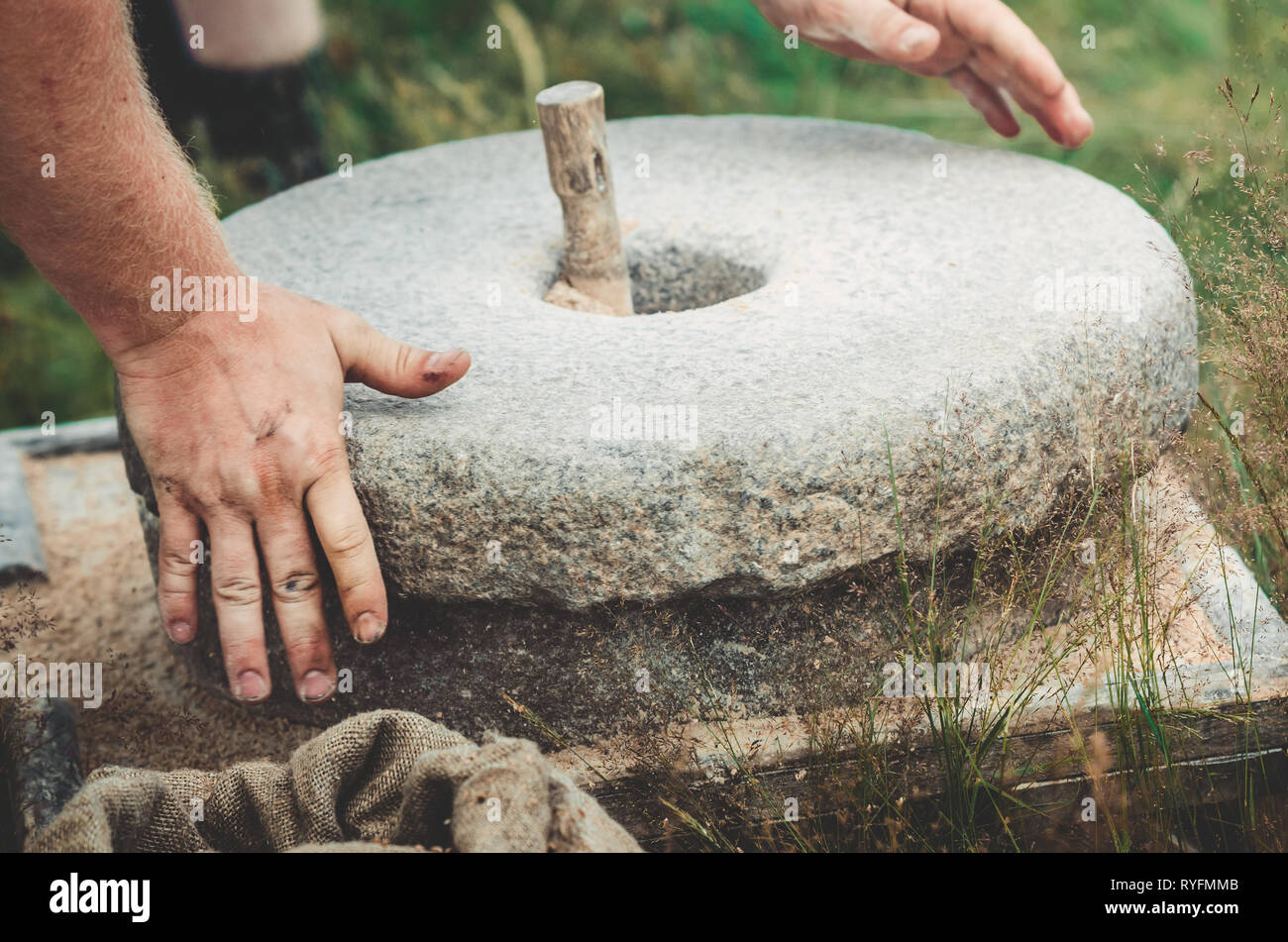 Die alten quern Stein Hand Mühle mit Korn. Der Mann schleift das Getreide zu Mehl mit Hilfe einer Mühlstein. Männer Hände auf einem Mühlstein. Alte Stockfoto