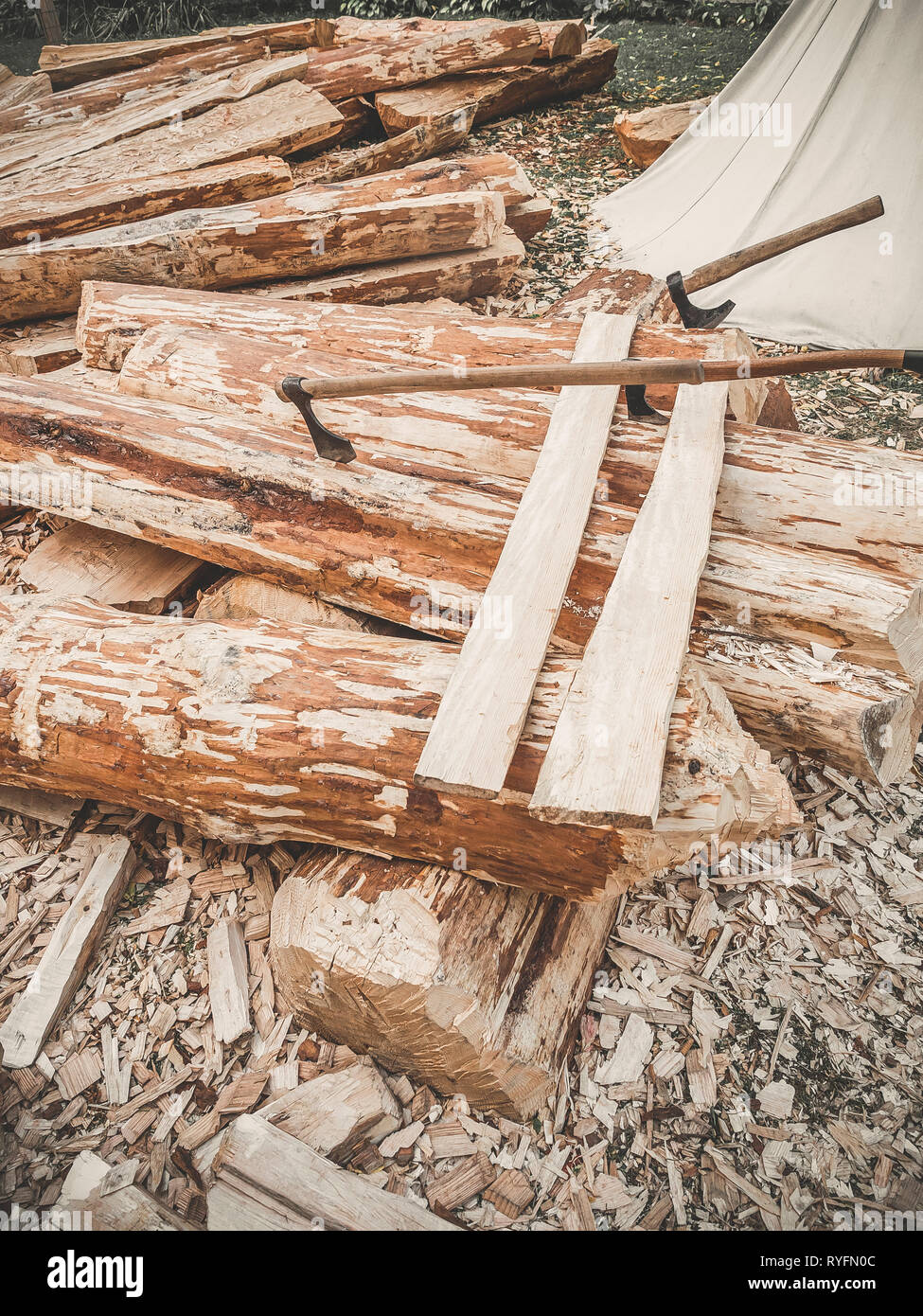 Baustelle. Brennholz mit Achsen auf einer Art. Viele Protokolle Holzbrett und drei Achsen outdoor. Bau eines hölzernen Barke. Stockfoto