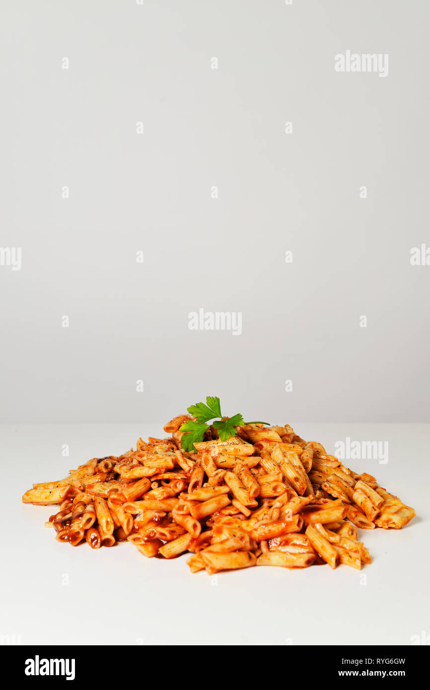 Nahaufnahme von einem Haufen ein Sortiment von verschiedenen gekochten Nudeln mit Tomatensoße und Kräutern auf einem weißen Tisch vor einem weißen Hintergrund diente, mit einem bl Stockfoto