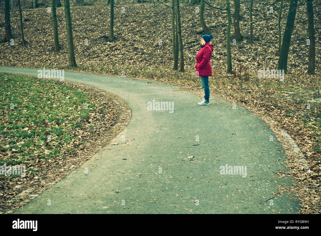 Frau im roten Mantel und Blau strick Hut stehen auf einer Straße in der Natur, mit Blick auf die Zukunft optimistisch in die Zukunft Stockfoto