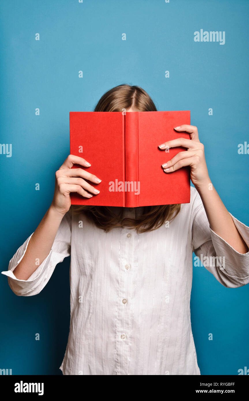 Blonde Mädchen hinter einem roten Buch ausblenden Stockfoto