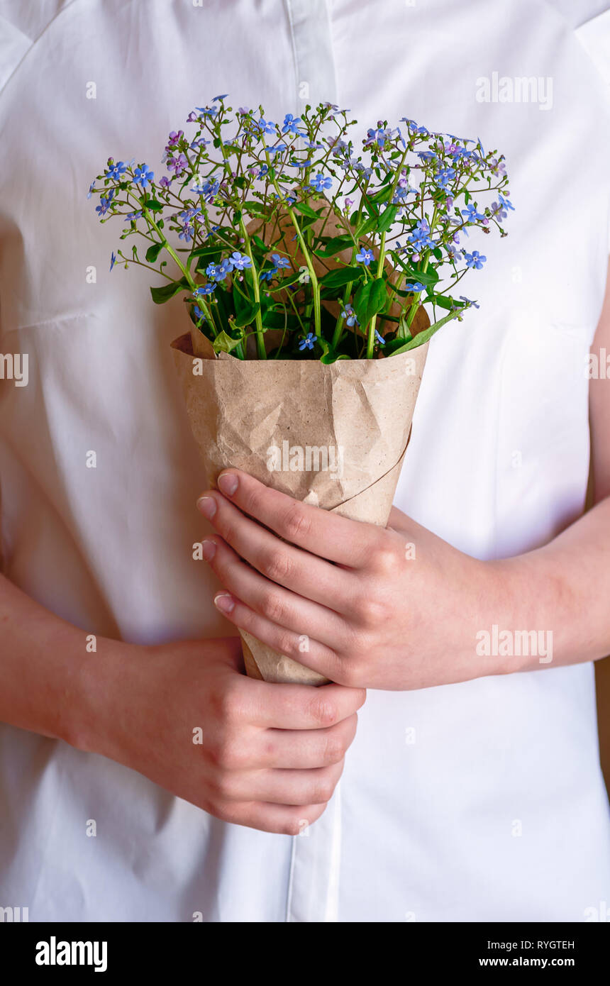Einen Strauß Vergissmeinnicht in den Händen der Mädchen, close-up. Frau mit einem Blumenstrauß mit Vergißmeinnicht Blumen. Die Idee der Frühling Spiel Stockfotografie