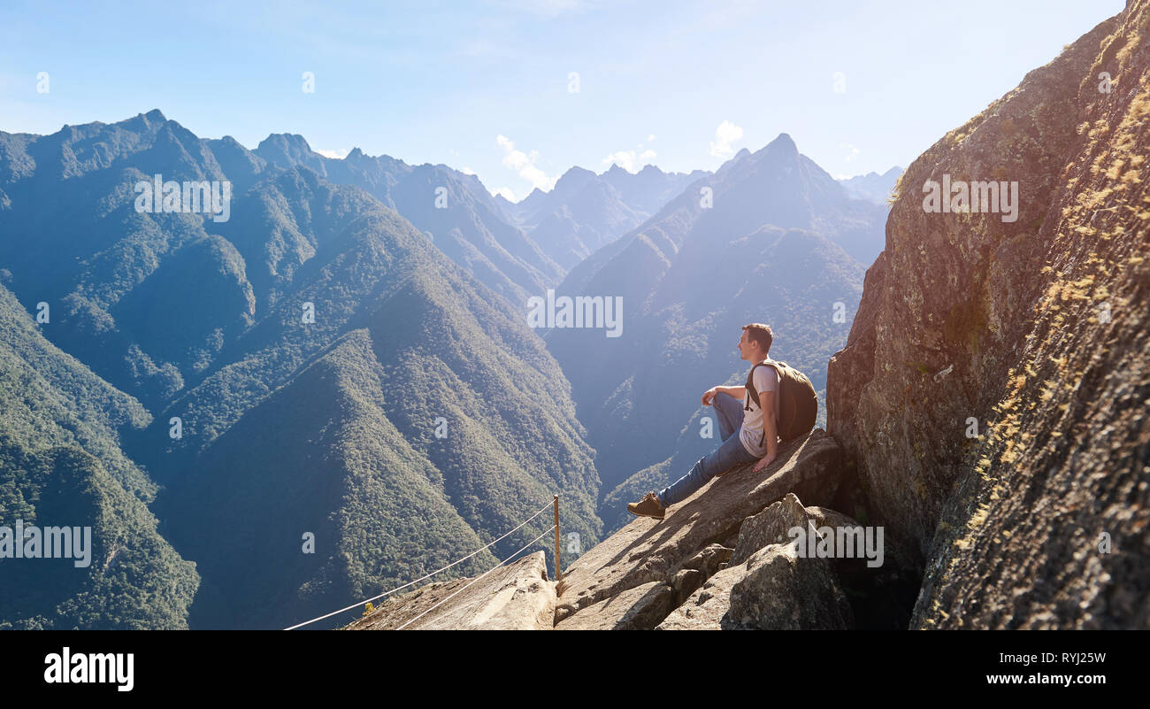 Ein junger Mann am Rande Klippe in Berg Hintergrund sitzen Stockfoto