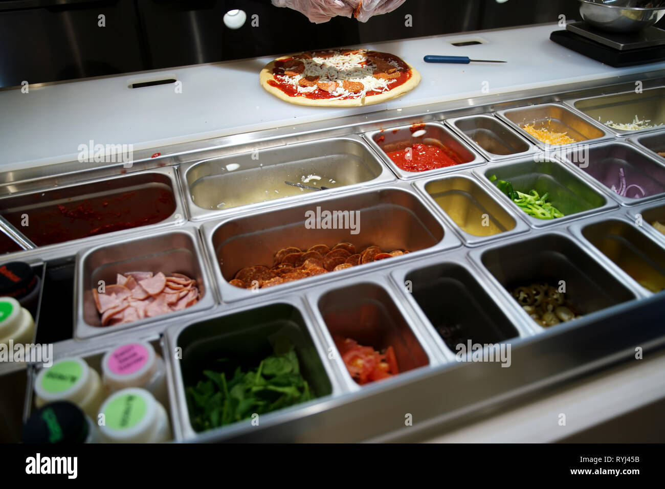 Hände in Handschuhen, leckeren Belag auf eine Pizza. Stockfoto