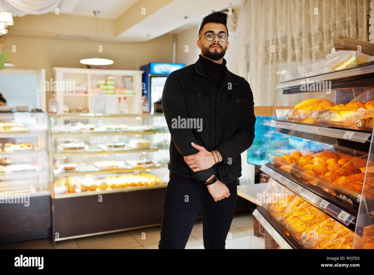 Arabischer mann Verschleiß auf schwarze Jeans Jacke und Brillen in Cafe wählen Bäckerei. Elegantes und Modisches arabischen Modell Kerl. Stockfoto