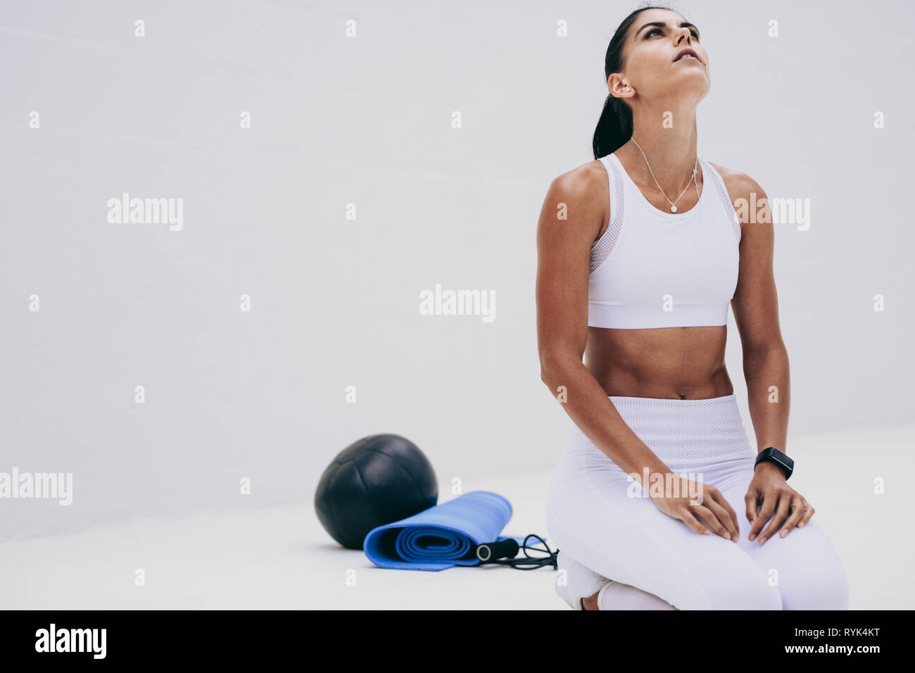 Fitnesstraining-Frau, die auf dem Boden sitzt und aufblickt. Eine Frau, die mit ihren Fitnessgeräten neben ihr Fitnesstraining macht. Stockfoto