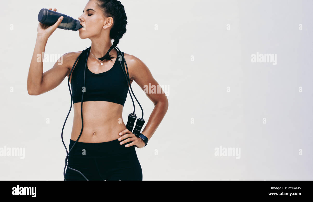 Frau in Fitnesskleidung, die eine Pause vom Workout-Trinkwasser macht. Fitness-Frau steht und trinkt Wasser aus einer Flasche mit Seilspringen Stockfoto