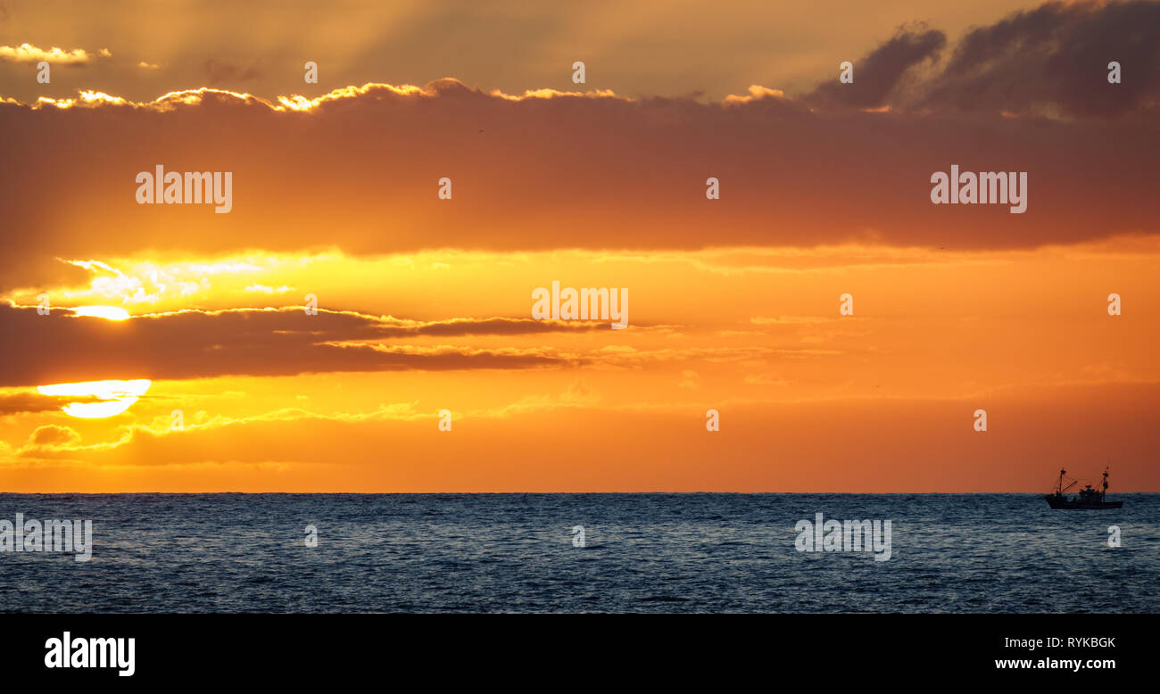 Fischerboot saling der Sonne am Horizont bei Sonnenuntergang Stockfoto