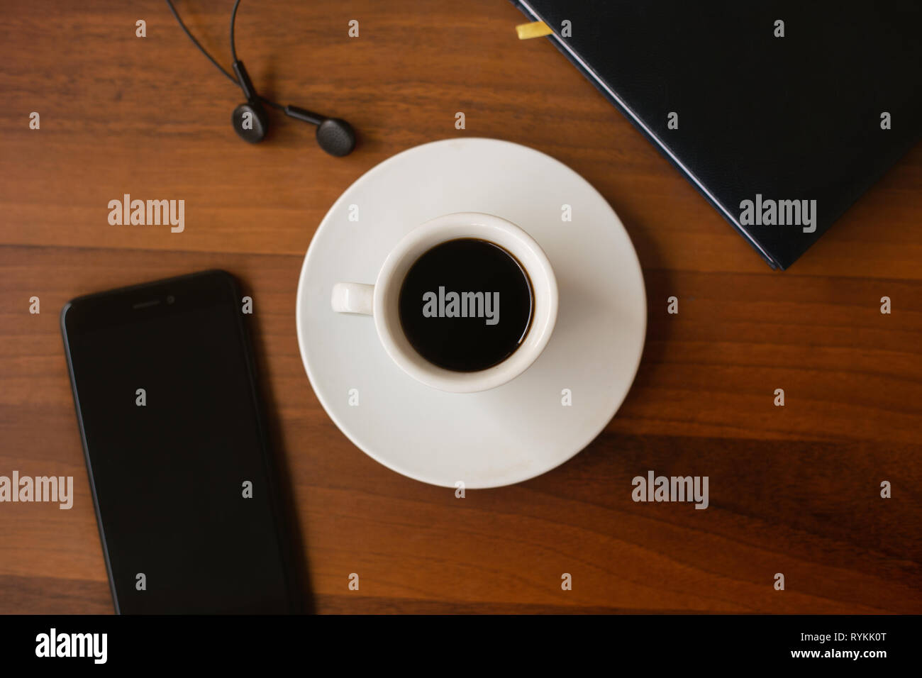 Ansicht von oben Tasse schwarzen Kaffee (Espressino), Agenda, Ohrhörer und Smartphone auf einen hölzernen Tisch. Office Konzept. Stockfoto