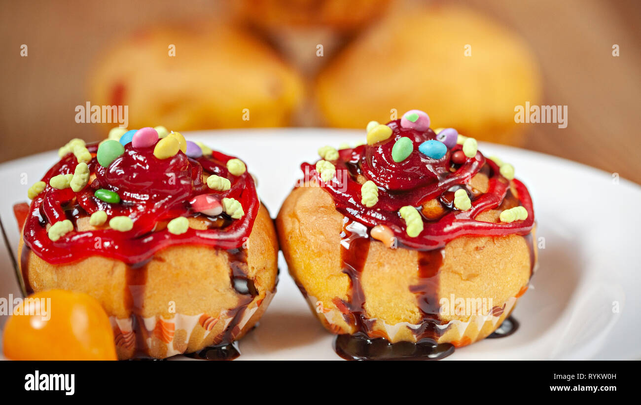 Close-up garniert Muffins mit den Belag von Süßigkeiten, Marmelade und dunkler Schokolade Sirup in weiße Platte mit poha Beeren auf hölzernen Tisch Stockfoto