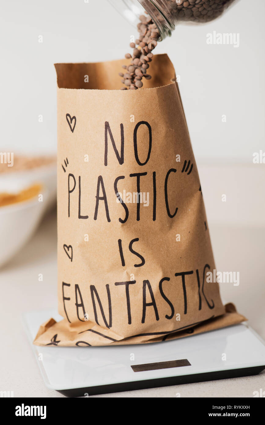 Nahaufnahme von einer braunen Papiertüte auf einer elektronischen Waage, erfüllt mit trockenen Linsen, mit dem Text keine Kunststoff ist fantastisch geschrieben, auf einem weißen St Stockfoto
