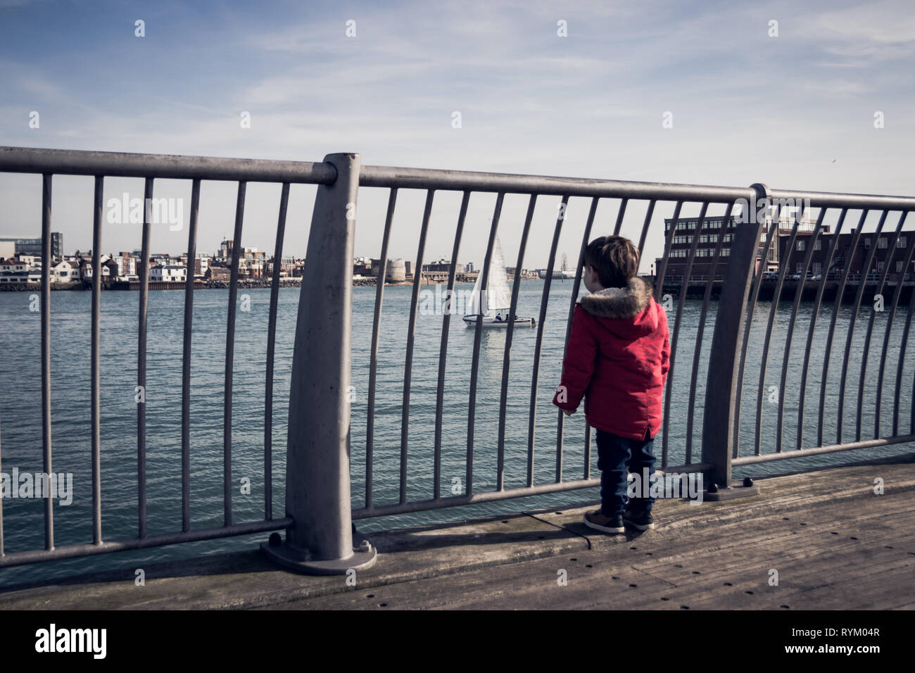 Kleine Jungen im roten Mantel an Boote und Yachten Portsmouth Harbour Blick von der Brücke in Gosport, Großbritannien Stockfoto