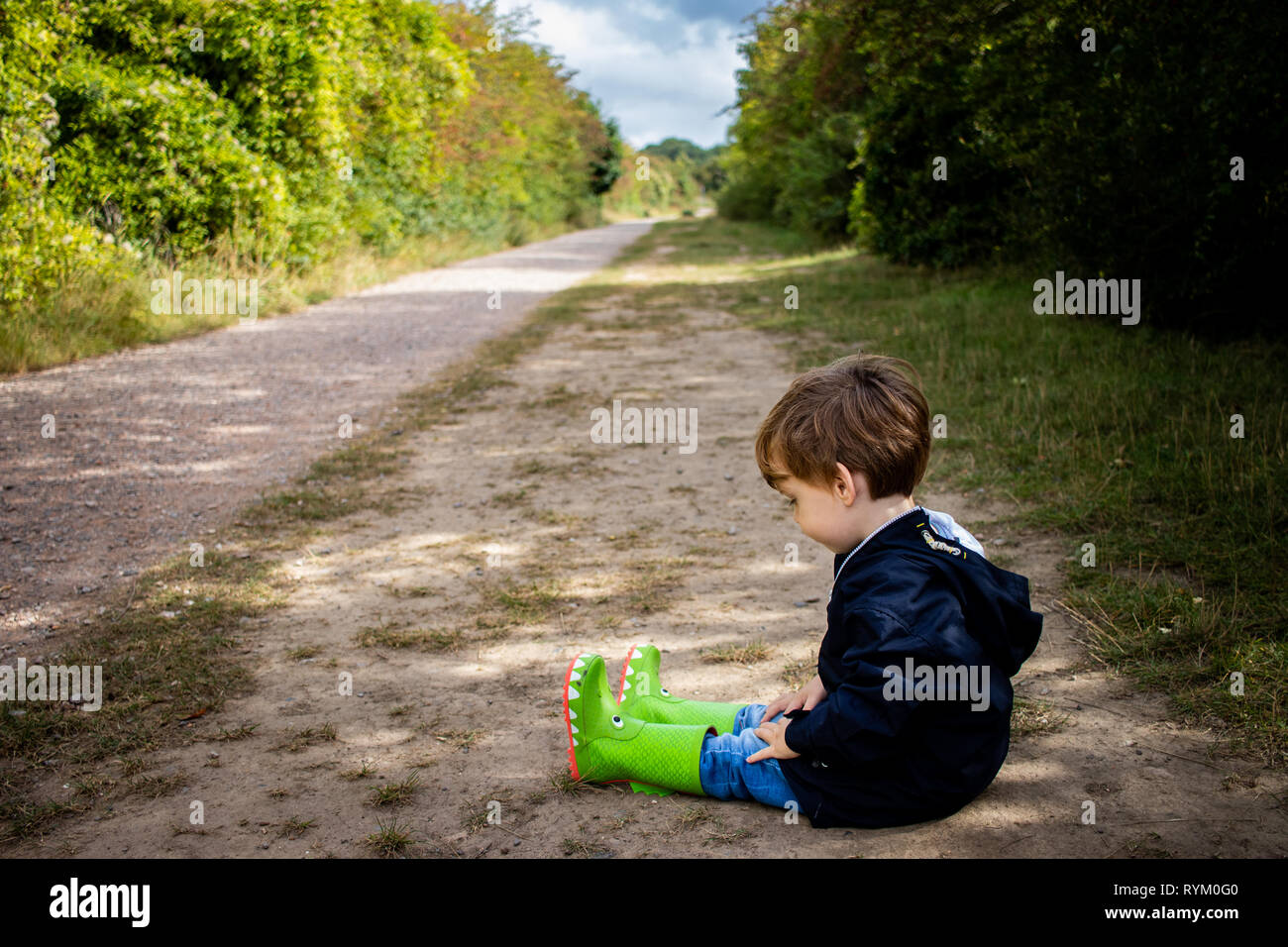 Kleiner Junge saß auf dem Boden auf Country Track tragen Gummistiefel Stockfoto