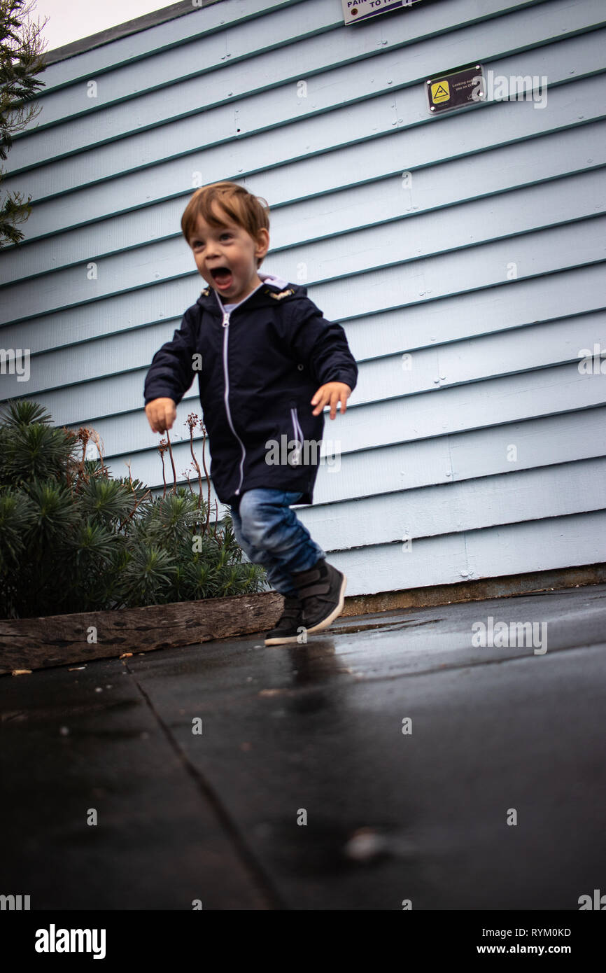 Kleiner Junge läuft durch Pfützen und lächelnd Stockfoto