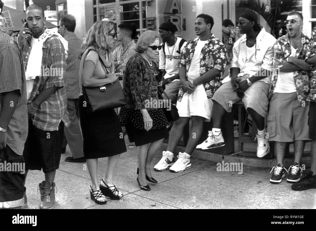 South Beach Ocean Drive Miami Florida 1990er USA. Zwei gestresste aussehende Geschäftsfrauen drängen durch eine Menge junger afroamerikanischer Männer, die während der Sommerferien aushängen. 1999 HOMER SYKES Stockfoto