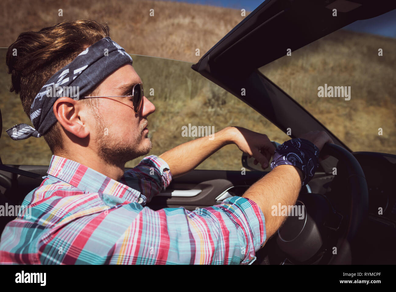 Stilvolle Mann in Kopfbügel und bunten T-Shirt fahren Cabrio Auto, Seitenansicht. Attraktiver Kerl mit Road Trip im Sommer sonnigen Tag in Kalifornien, USA. Stockfoto