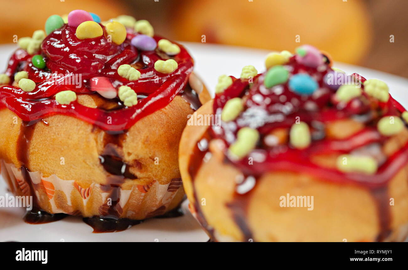 Close-up garniert Muffins mit den Belag von Süßigkeiten, Marmelade und dunkler Schokolade Sirup in weiße Platte mit poha Beeren auf hölzernen Tisch Stockfoto