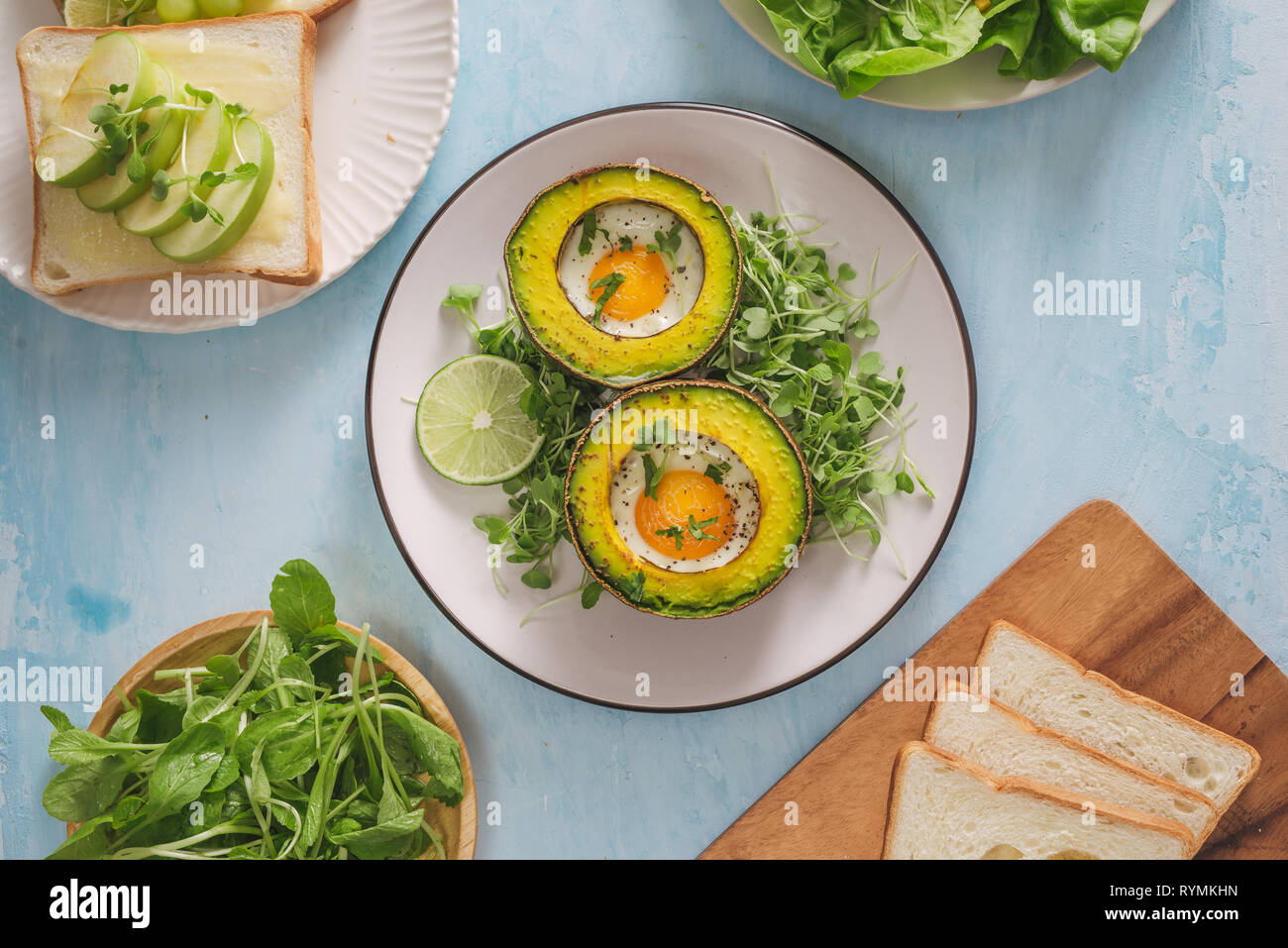 Gesunde vegane Frühstück. Ernährung. Gebackene Avocado mit Ei und frischem Salat aus Rucola, Toast und Butter. Auf eine weiße Marmorplatte, einem konkreten Leuchttisch. Stockfoto
