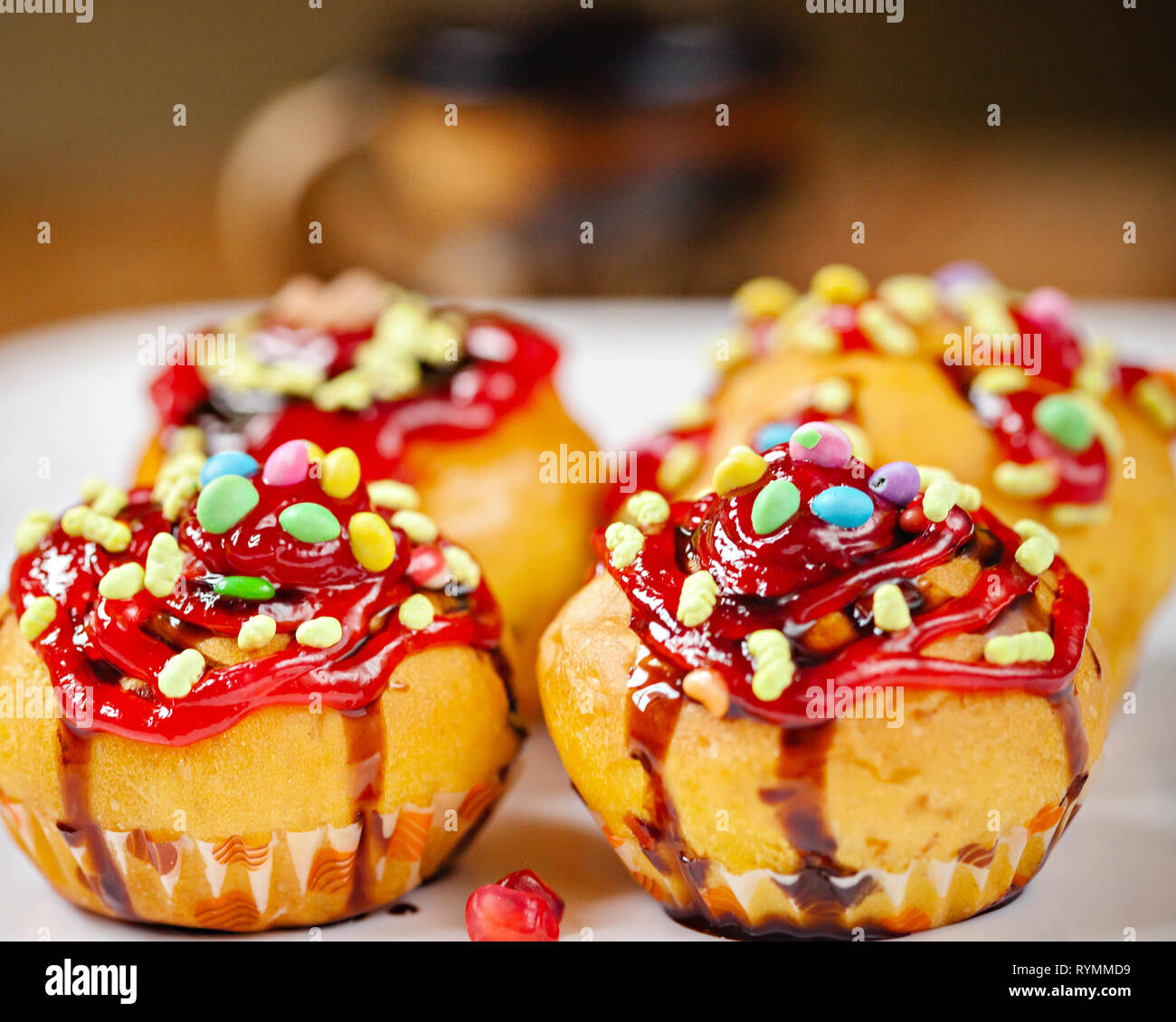 Close-up garniert Muffins mit den Belag von Süßigkeiten, Marmelade und dunkler Schokolade Sirup in weiße Platte mit poha Beeren auf hölzernen Tisch Stockfoto