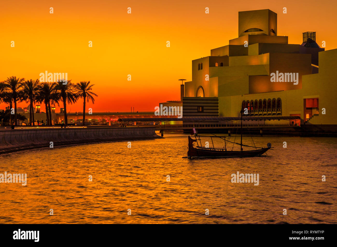 Malerische Küste Landschaft von Doha Bay Park mit Palmen, einer Dhow und Wahrzeichen in bunten Sonnenuntergang Himmel. Urbane Stadtbild von Doha, Hauptstadt von Katar Stockfoto