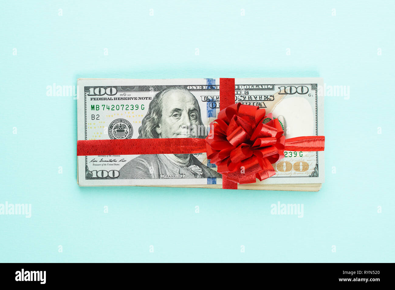 US Dollar Geld Bargeld mit rotem Band und Bogen auf blauem Hintergrund. 100 amerikanische Dollar banknote Geschenk gewinn Konzept Stockfoto