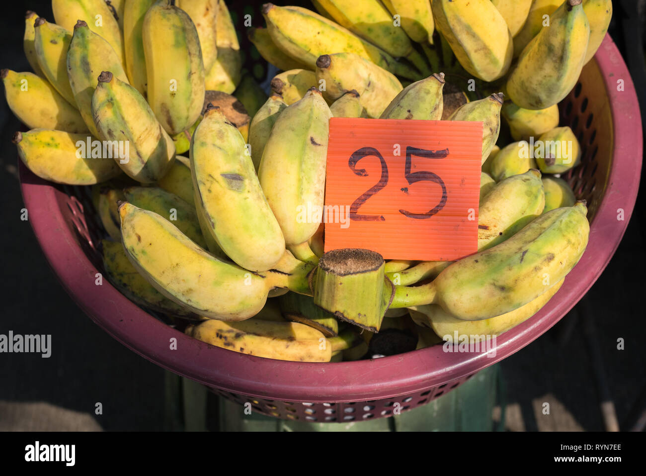 Bananen in einem Korb mit Preisschild 25 (Thai Baht) beleuchtet mit Sonne am Markt. Stockfoto