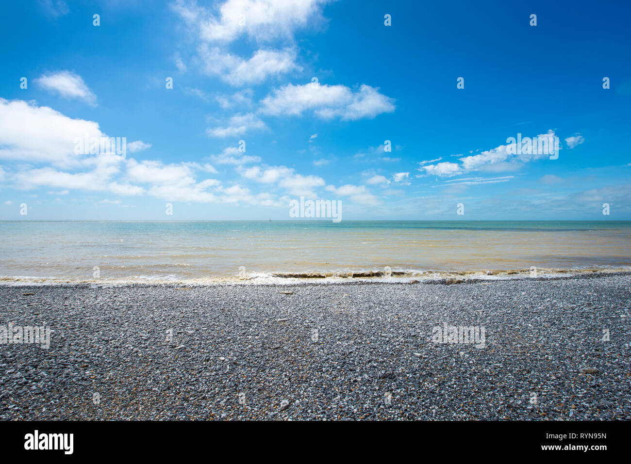 Weitwinkel von leeren Kieselstrand mit Blick über das Meer, eine kleine Breaker, aalen sich in der Sonne mit blauem Himmel Stockfoto