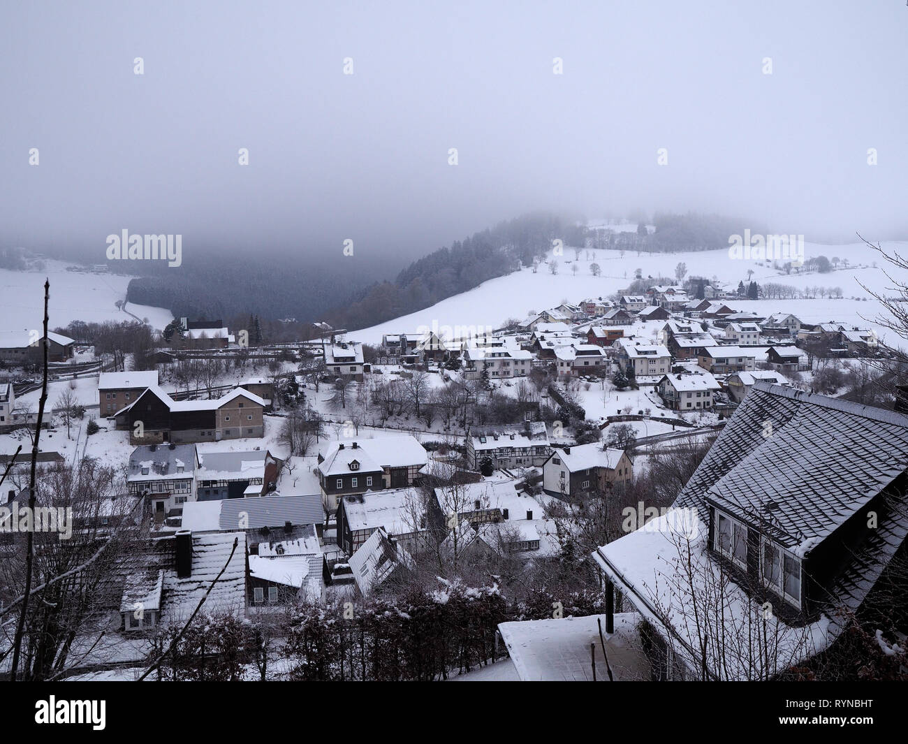 Sauerland - Blick über verschneite Kleinstadt mit bewaldeten Hügeln und tief hängenden Wolken im Hintergrund Stockfoto